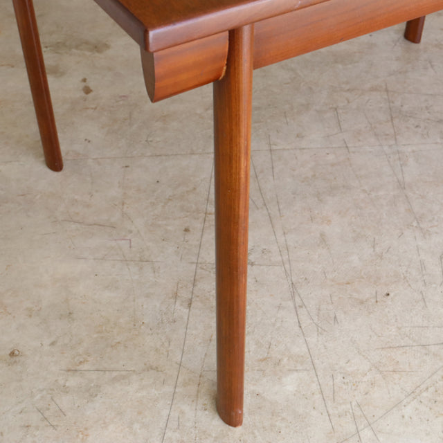 Mid-century British teak dining table leg with smooth wood grain, rounded edge, and tapered cylindrical form.