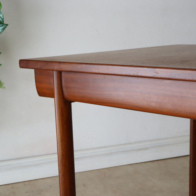 Mid-century British vintage teak dining table with rich wood grain and rounded tapered legs.