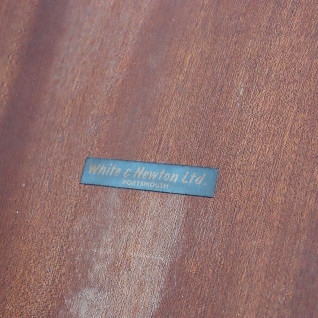 Close-up of vintage teak wood grain with White & Newton Ltd British mid-century Denmark label on dining table surface.