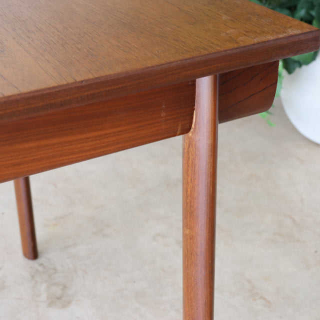 Vintage British mid-century teak dining table corner with smooth wood grain and tapered round legs.