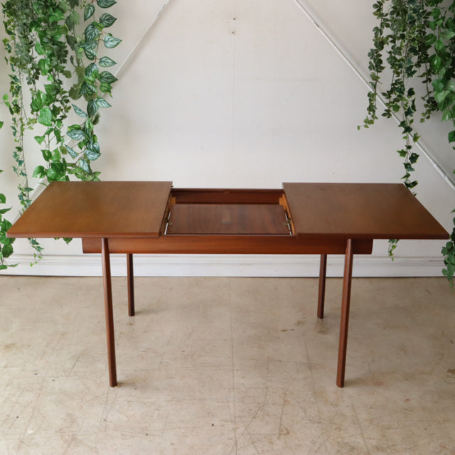 Mid-century British teak dining table by Whiteandnewton with extendable leaves, slender tapered legs, and rich wood grain.
