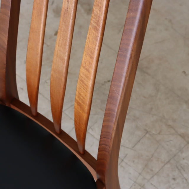 Close-up of vintage teak dining chair backrest with mid-century British design, smooth wood grain and black seat cushion,.
