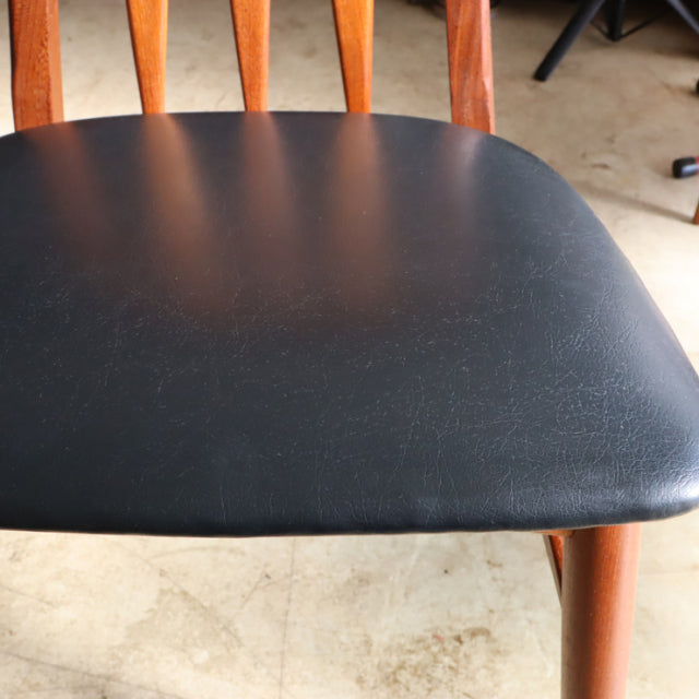 Close-up of vintage Danish teak dining chair with black leather seat, mid-century British style legs, and visible wood grain .