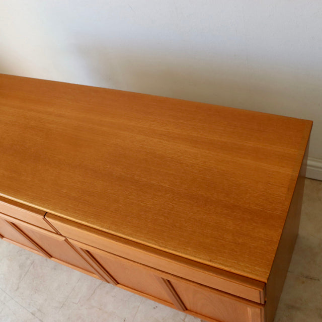 British mid-century teak McIntosh sideboard with smooth wood grain, clean lines, and sleek vertical handles.