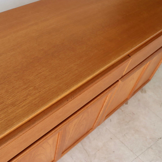 Mid-century British McIntosh teak sideboard with smooth wood grain top and sculpted door panels in vintage Denmark style.