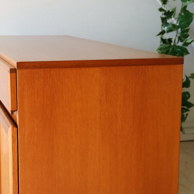 Vintage British McIntosh mid-century teak sideboard with smooth wood grain and clean lines, sturdy legs visible.