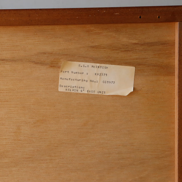 Close-up of vintage British McIntosh sideboard label on smooth teak wood interior panel.