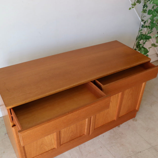 Vintage British mid-century McIntosh teak sideboard with smooth wood grain, sliding drawers, and paneled doors.