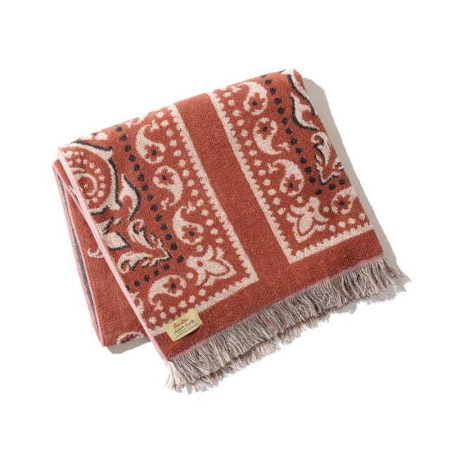 Red bandana-patterned cotton pile blanket with beige fringed edges and a small beige brand tag.