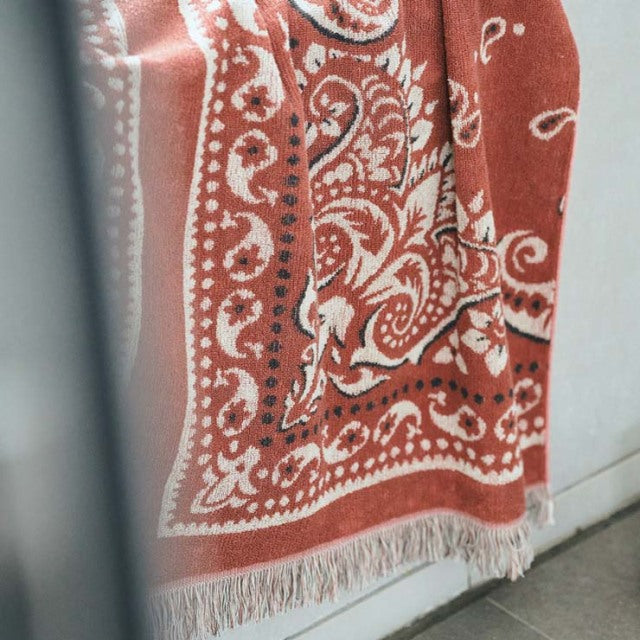 Vintage red bandana-patterned cotton pile blanket with intricate white paisley designs and fringed edges, styled in a.