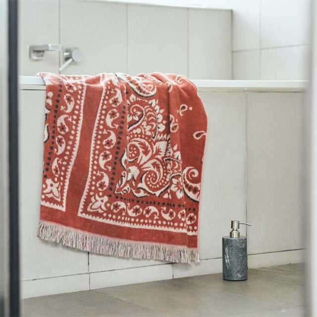 Red cotton pile blanket with white bandana print and fringe detail hanging on mid-century teak furniture in a bright,.