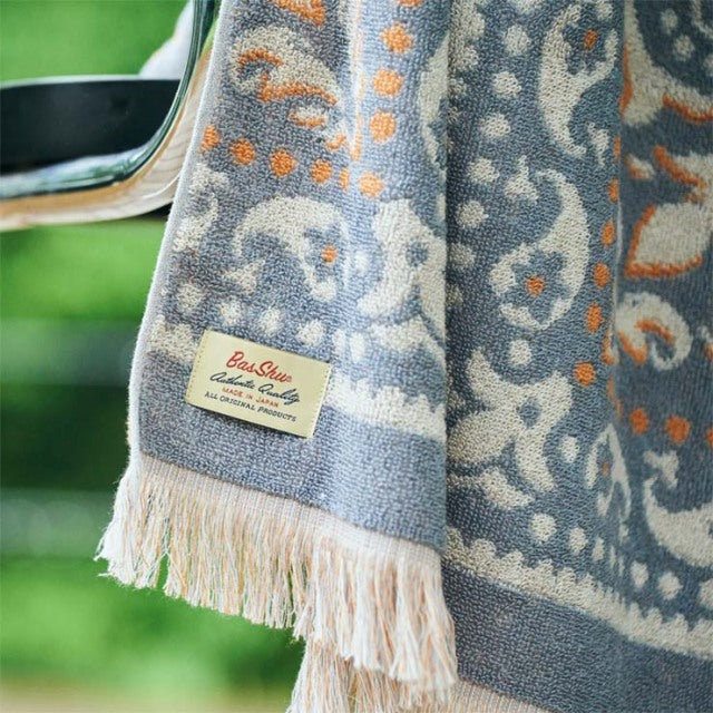 Gray and orange vintage-style cotton pile blanket with intricate paisley bandana pattern and fringed edges, labeled Basshu.