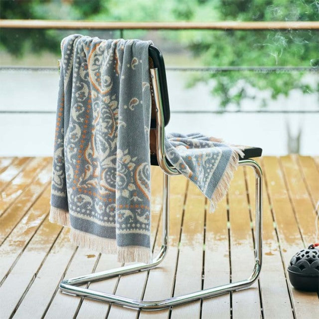 Mid-century steel frame chair with black leather seat, teak table edge visible, gray and white patterned cotton pile blanket .