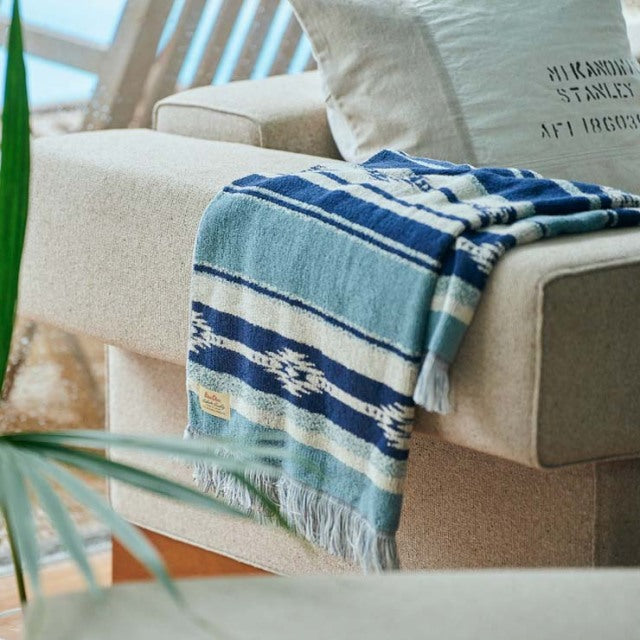 Blue and white Native Border cotton pile blanket draped over beige mid-century sofa with teak legs, British and Danish.