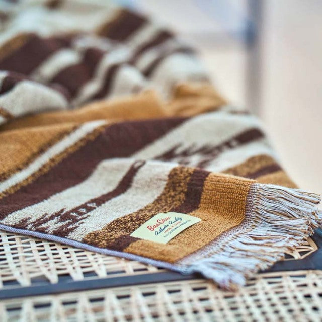 Brown and beige striped cotton pile blanket with fringed edges draped over vintage teak mid-century British furniture with.