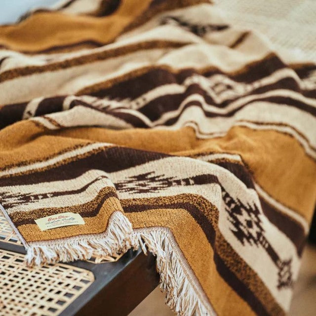 Brown and cream Native Border cotton pile blanket draped over vintage teak mid-century Danish chair with woven cane seat and .