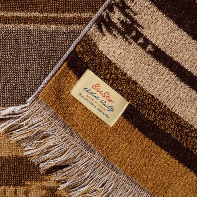 Brown cotton pile blanket with native border design, fringed edges, and Basshu brand label crisp and clear.