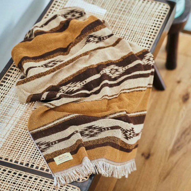 Brown and beige vintage cotton pile blanket with native border pattern draped over mid-century teak chair with woven cane.