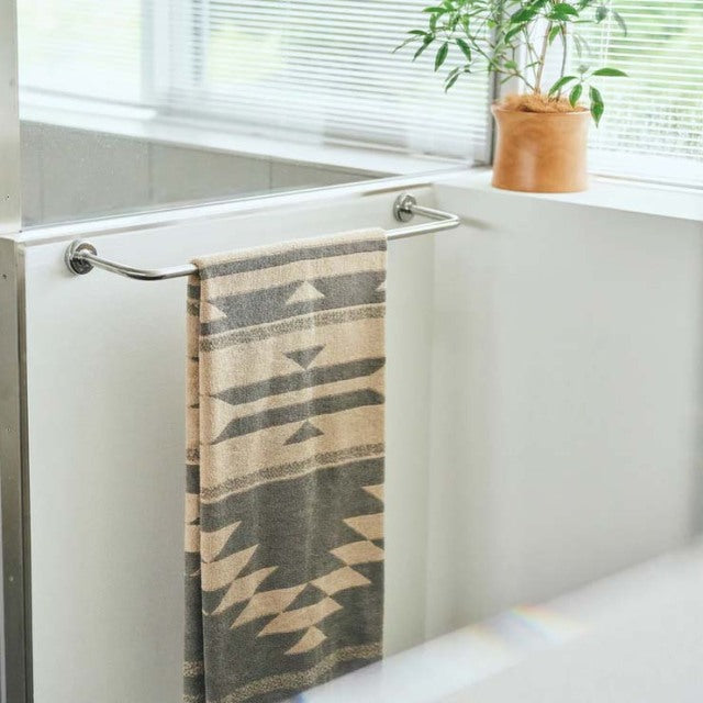 Mid-century British teak towel rack with sleek metal bars holding a beige Native motif cotton pile blanket, set against a.