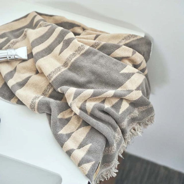 Beige cotton pile blanket with native geometric motif, soft texture, fringed edges, vintage-inspired design.