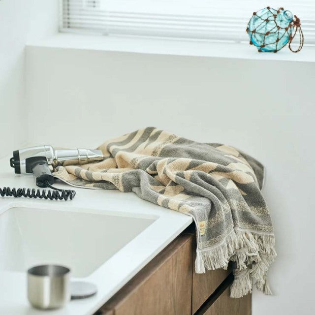 Beige cotton pile blanket with native motif draped over mid-century teak kitchen counter edge, featuring visible wood grain.