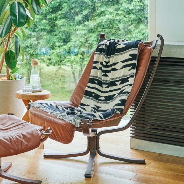 Mid-century teak lounge chair with curved leather cushions and black metal frame, draped with black and white Native motif.