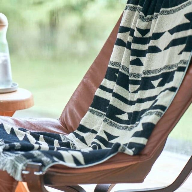 Mid-century British teak lounge chair with sleek wood grain frame draped with black and white vintage Native Motif cotton.