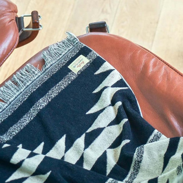Black and white Native motif cotton pile blanket draped over vintage mid-century teak British chair with rich wood grain and .
