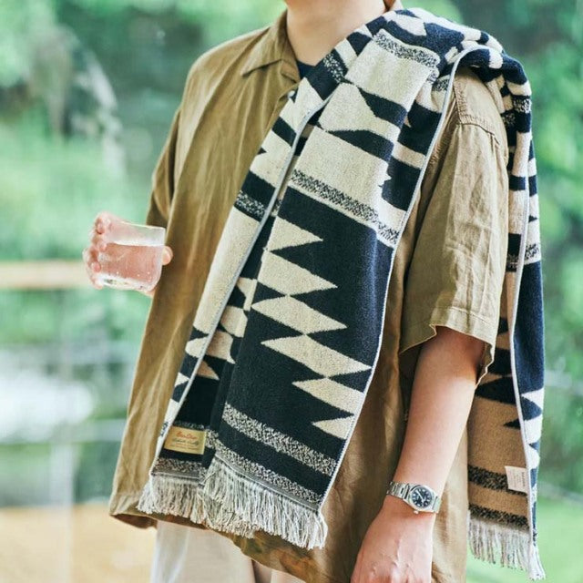 Black and white cotton pile blanket with Native motif draped over arm, featuring fringe edges and Basshu label, held by.