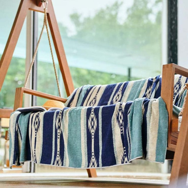 Blue and beige Native Border cotton pile blanket draped over mid-century teak armchair with clean lines and warm wood grain.