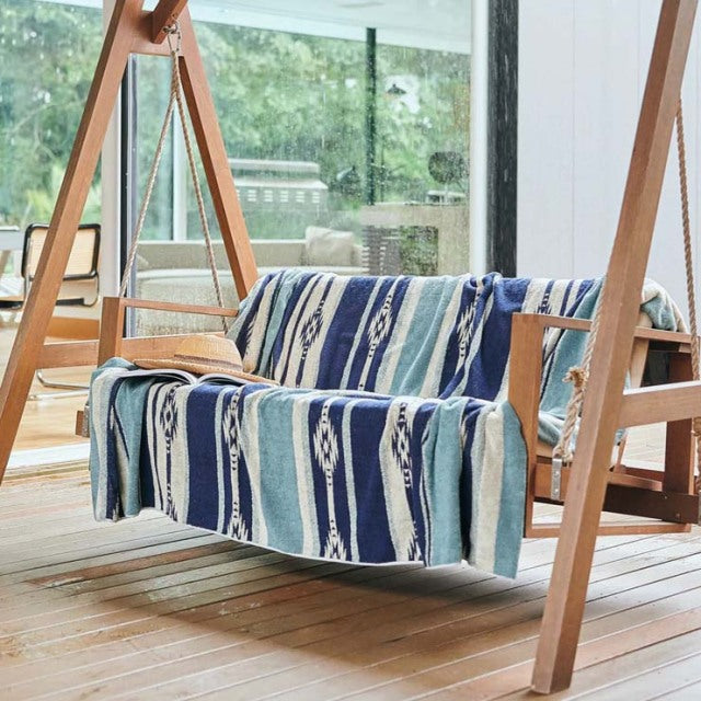 Mid-century British teak swing chair with visible wood grain, draped with blue Native Border cotton pile blanket.