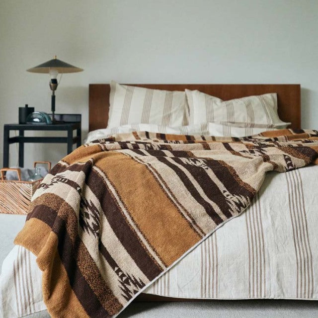 Mid-century teak bed with clean lines, dressed in a brown native border cotton pile blanket and striped white bedding,.