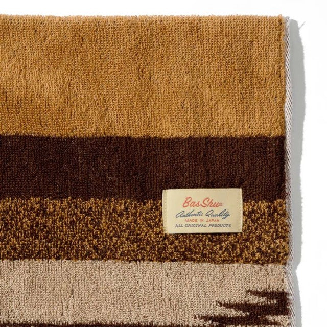 Brown cotton pile blanket with native border design, textured stripes in beige, brown, and rust, featuring a branded Basshu.