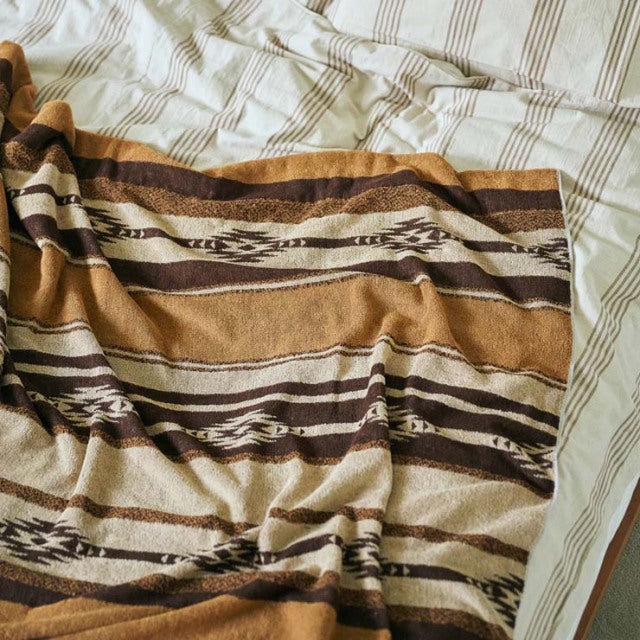 Brown and beige vintage cotton pile blanket with native border pattern draped over mid-century striped bedding.