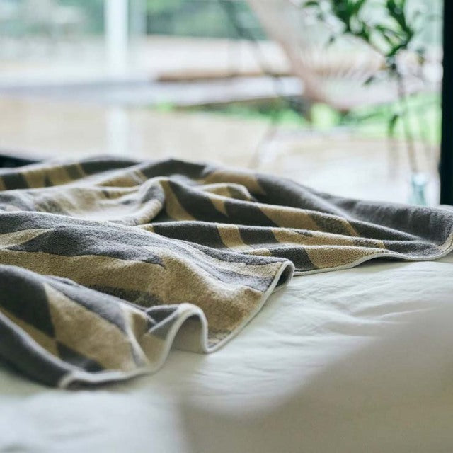 Beige cotton pile blanket with native motif draped over white bedding in bright, natural light.