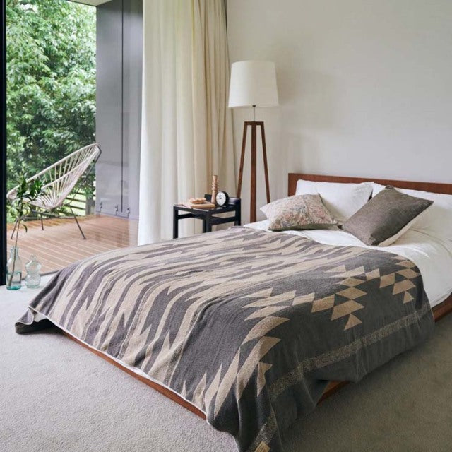 Mid-century teak bed with clean lines, topped with a beige vintage cotton pile blanket featuring a native motif,.