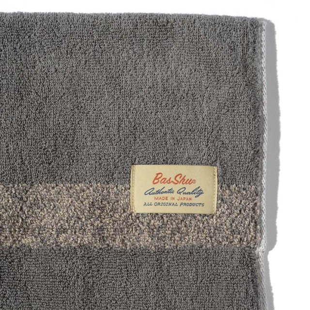 Beige cotton pile blanket with textured stripe and cream Basshu brand label on corner.