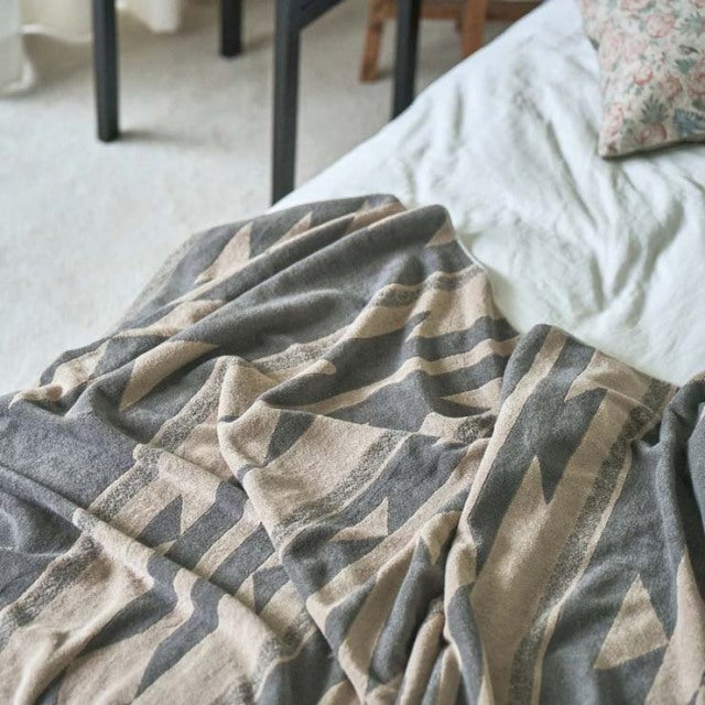 Beige cotton pile blanket with native-inspired dark brown geometric patterns draped over bed linens.