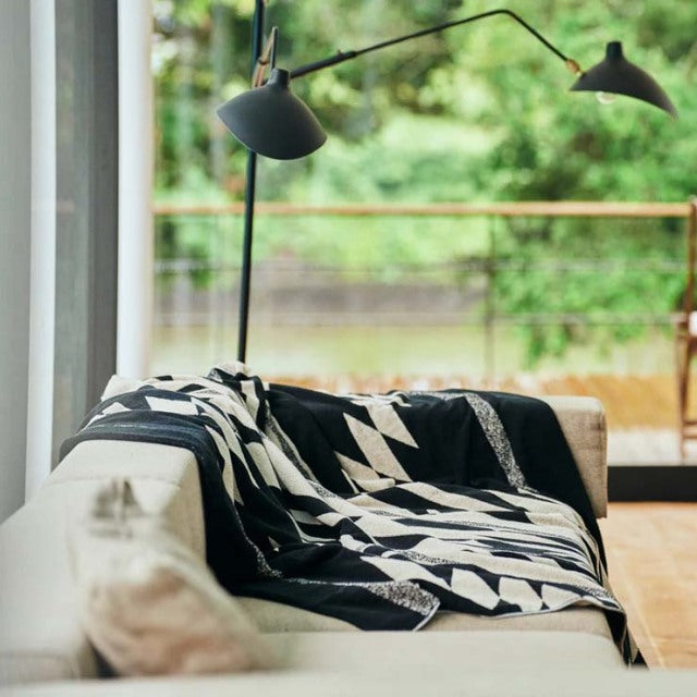 Mid-century teak sofa with visible wood grain, draped with a black and white Native motif cotton pile blanket, set beside a.