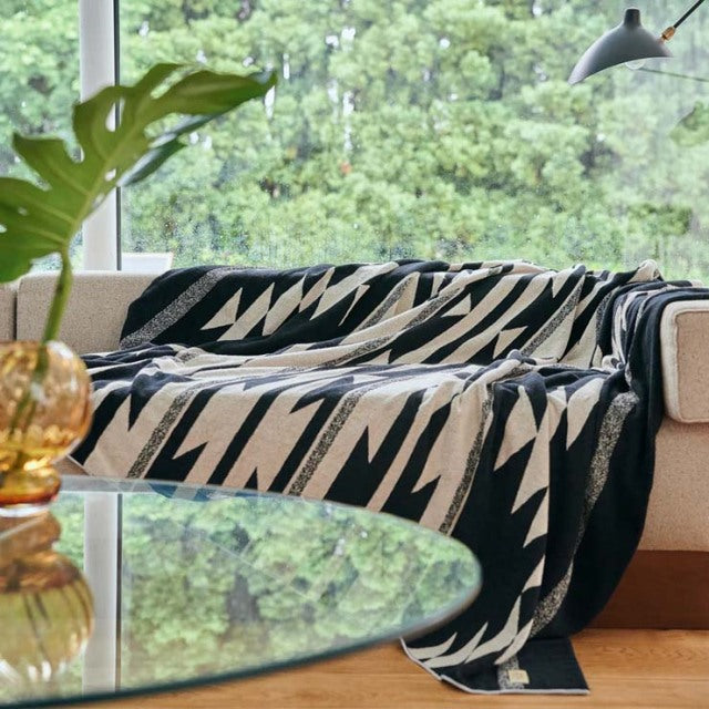 Black and beige Native Motif cotton pile blanket draped over beige mid-century sofa with teak legs, vintage British vibe,.