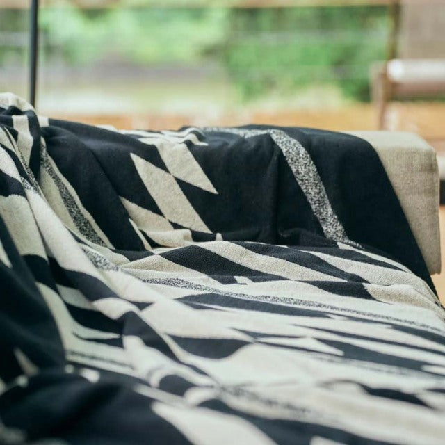 Black and white Native motif cotton pile blanket draped over beige sofa in cozy setting.