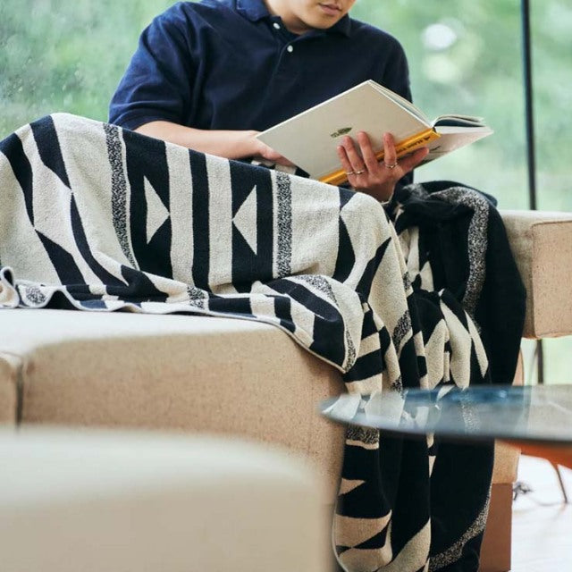 Black and white native motif cotton pile blanket draped over beige mid-century teak sofa with visible wood grain and slender .