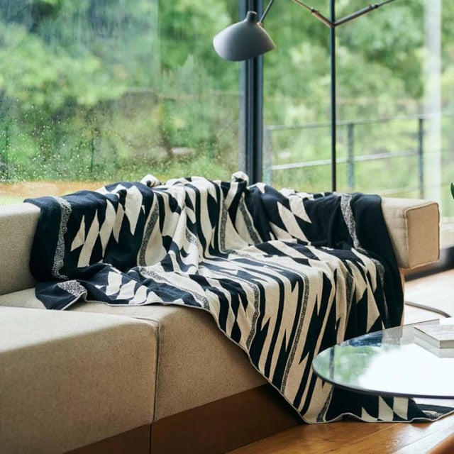 Mid-century British vintage teak sofa with clean lines draped in a black and cream Native motif cotton pile blanket, beside.