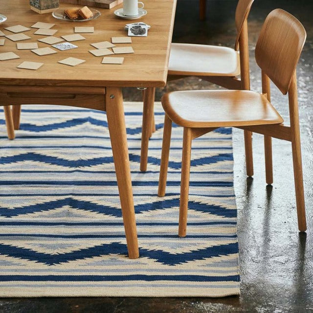Mid-century teak dining table and chairs with visible wood grain paired with a blue and white striped vintage cotton rug.