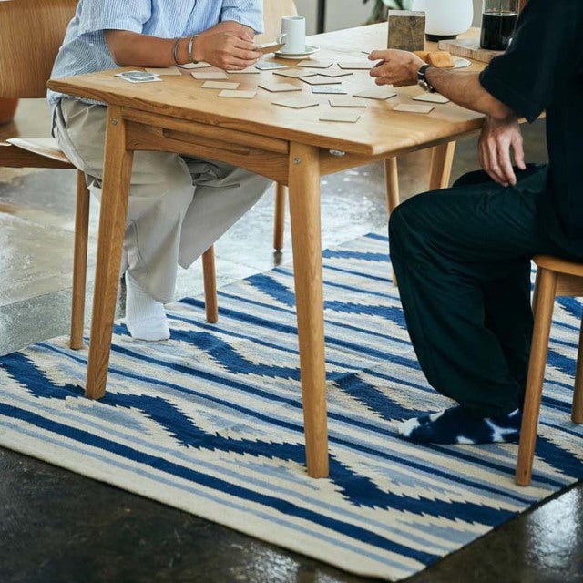 Mid-century teak dining table with tapered legs on vintage blue and white striped cotton rug.