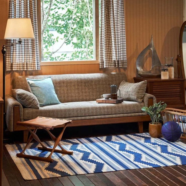 Mid-century British vintage teak sofa with woven fabric cushions, paired with teak sideboard and patterned Danish rug.
