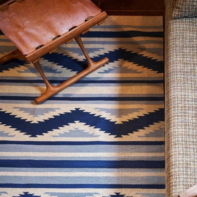 Mid-century teak wooden chair with leather seat on vintage British cotton rug featuring geometric navy and beige patterns,.