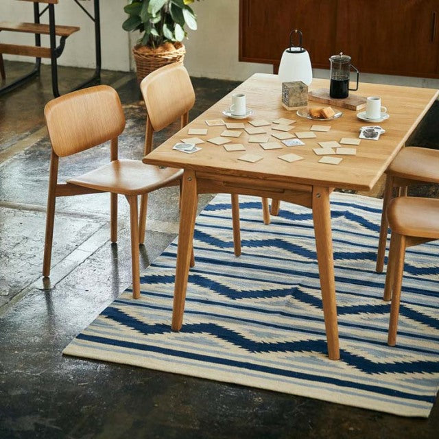 Mid-century teak dining table with clean lines and tapered legs on vintage British cotton rug, blue and white zigzag.