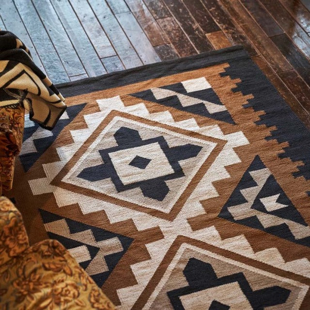 Vintage mid-century cotton rug with geometric patterns in black, brown, and beige on teak wooden floor.