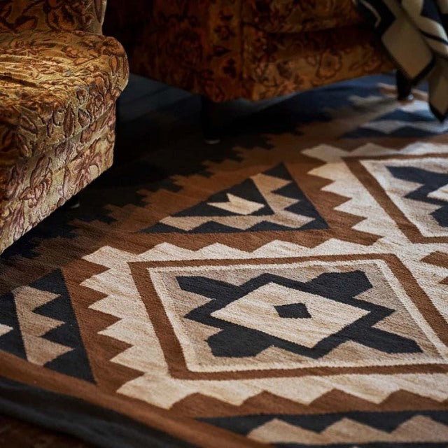Vintage mid-century teak furniture legs visible on patterned British-Denmark inspired cotton rug with geometric designs.